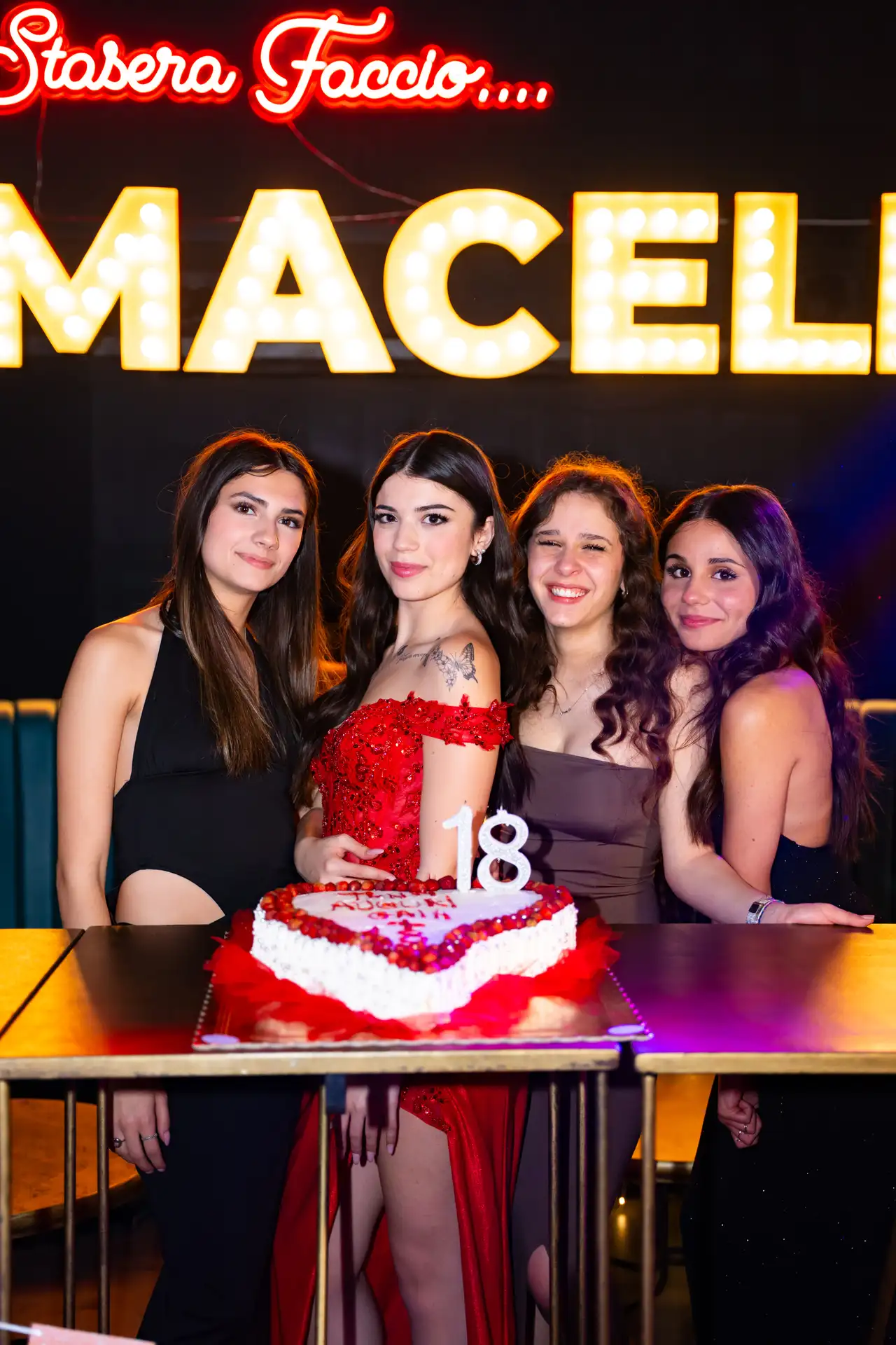 Gruppo di persone attorno a una torta di compleanno nel Clubbino, sotto l'insegna a lampadine