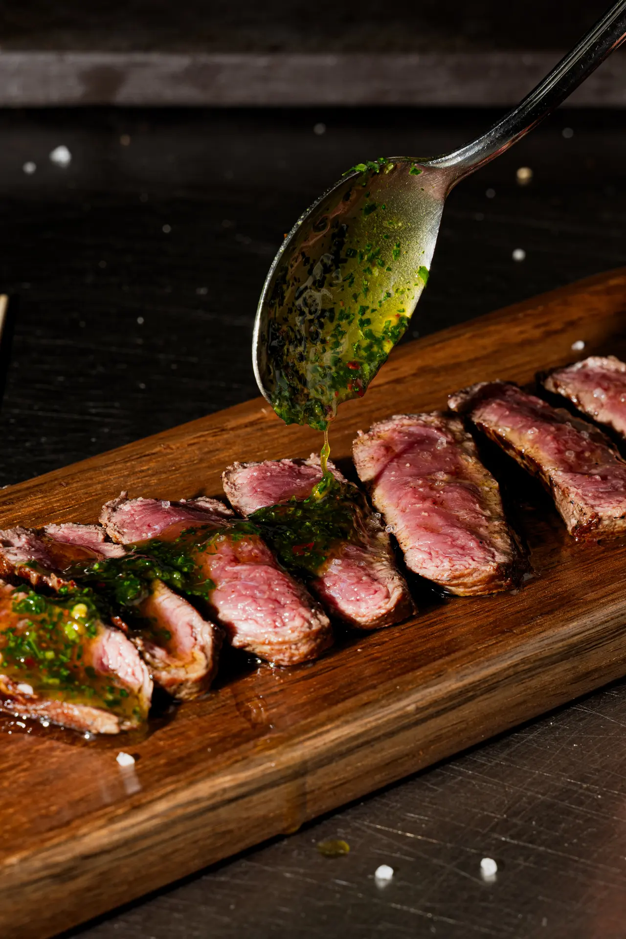 Tagliata di manzo affettata su un tagliere, con il chimichurri versato dal cucchiaio