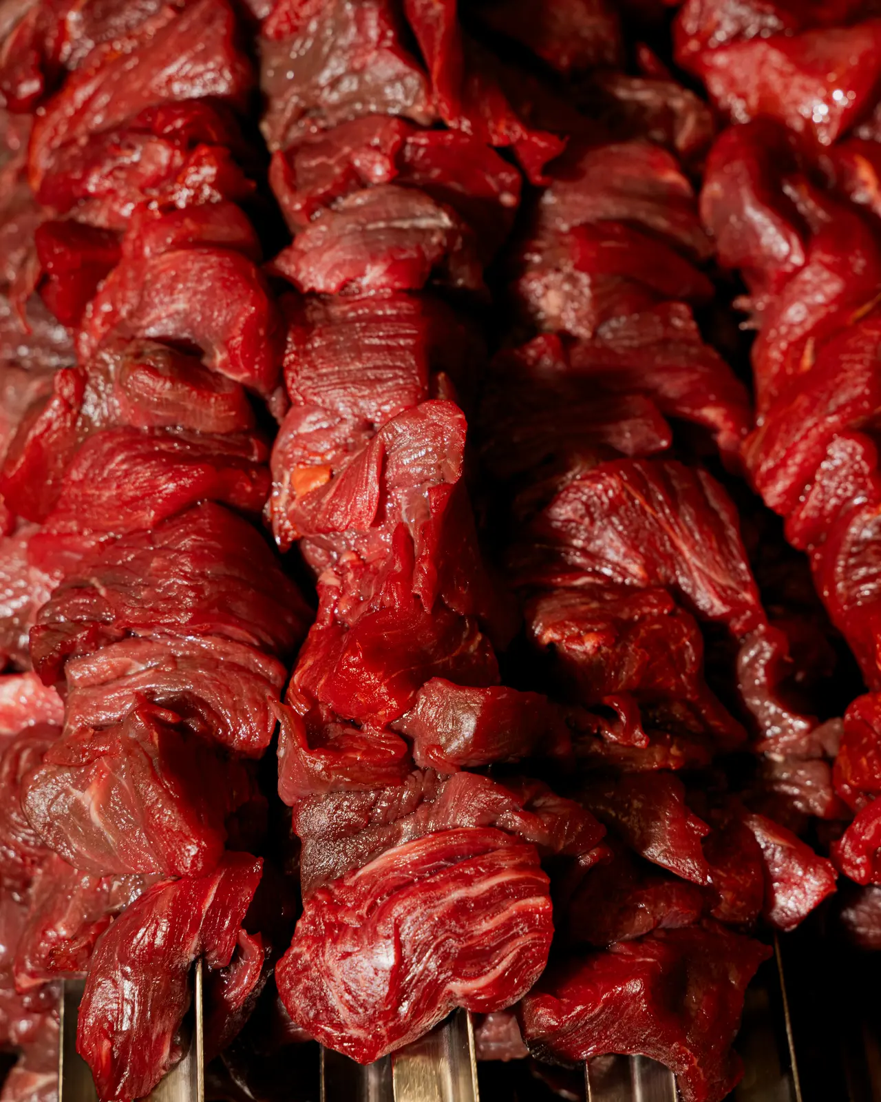 Spiedini di carne cruda marinata allineati fitti, in primo piano